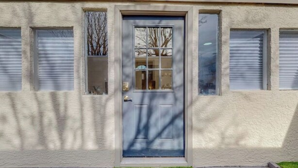 A building facade with a blue door, windows with blinds, and a small green lawn area.
