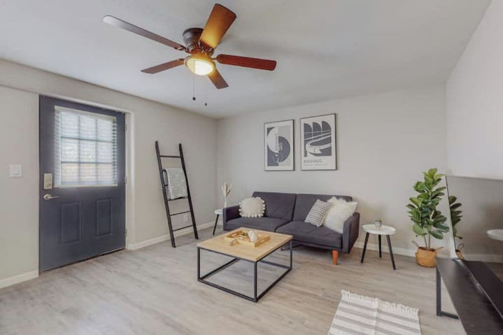 Ein modernes Wohnzimmer mit Deckenventilator, einer Couch, einem Couchtisch und einer Tür.