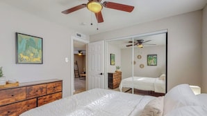 A bedroom with a bed, a dresser, a ceiling fan, and a door leading to another room.