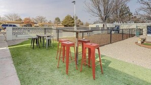 An outdoor seating area with a table and four red stools, surrounded by a low fence and a grassy lawn.