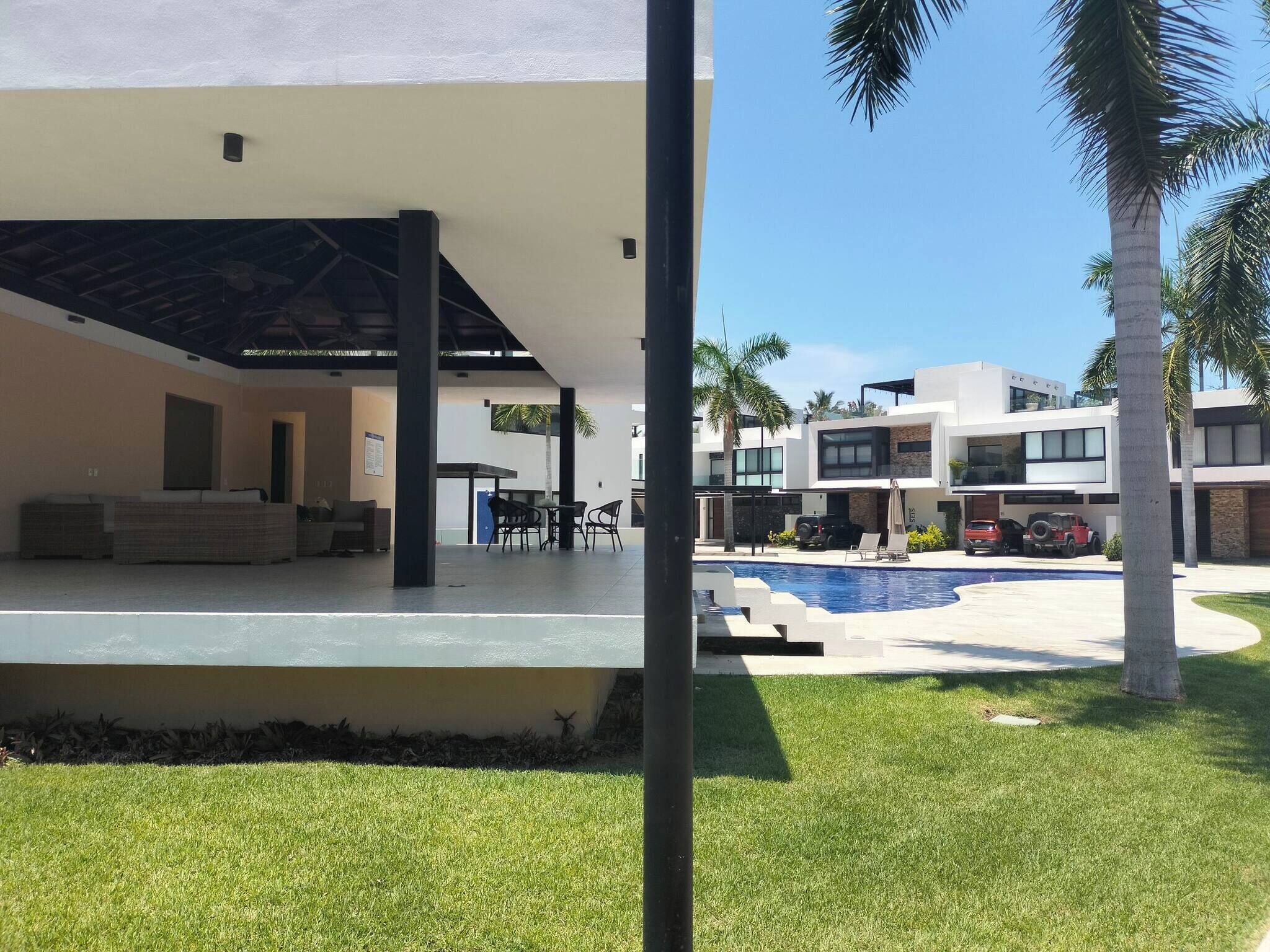 A modern building with a covered outdoor seating area, a swimming pool, and palm trees.