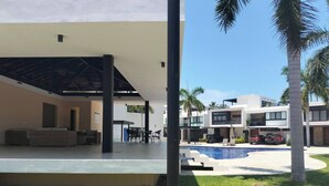 Un edificio moderno con una zona de estar exterior cubierta, piscina y palmeras.
