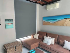 A living room with a brown sofa, a wicker chest, and a beach painting on the wall.