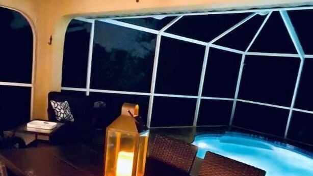 A dining area with a table, chairs, a lantern, and a view of a swimming pool at night. - Villa Gone Golfing (Rotonda West)