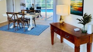 A spacious dining area with a large table and chairs, a hanging light fixture, and a view of a swimming pool through large windows. - Villa Gone Golfing (Rotonda West)