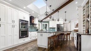 Une cuisine moderne avec des meubles blancs, un grand îlot central doté de tabourets et une verrière.
