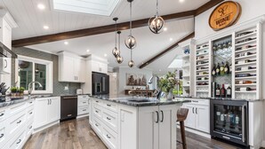 Une cuisine spacieuse avec des meubles blancs, un îlot central et un coin bar à vin doté d’étagères remplies de bouteilles de vin.