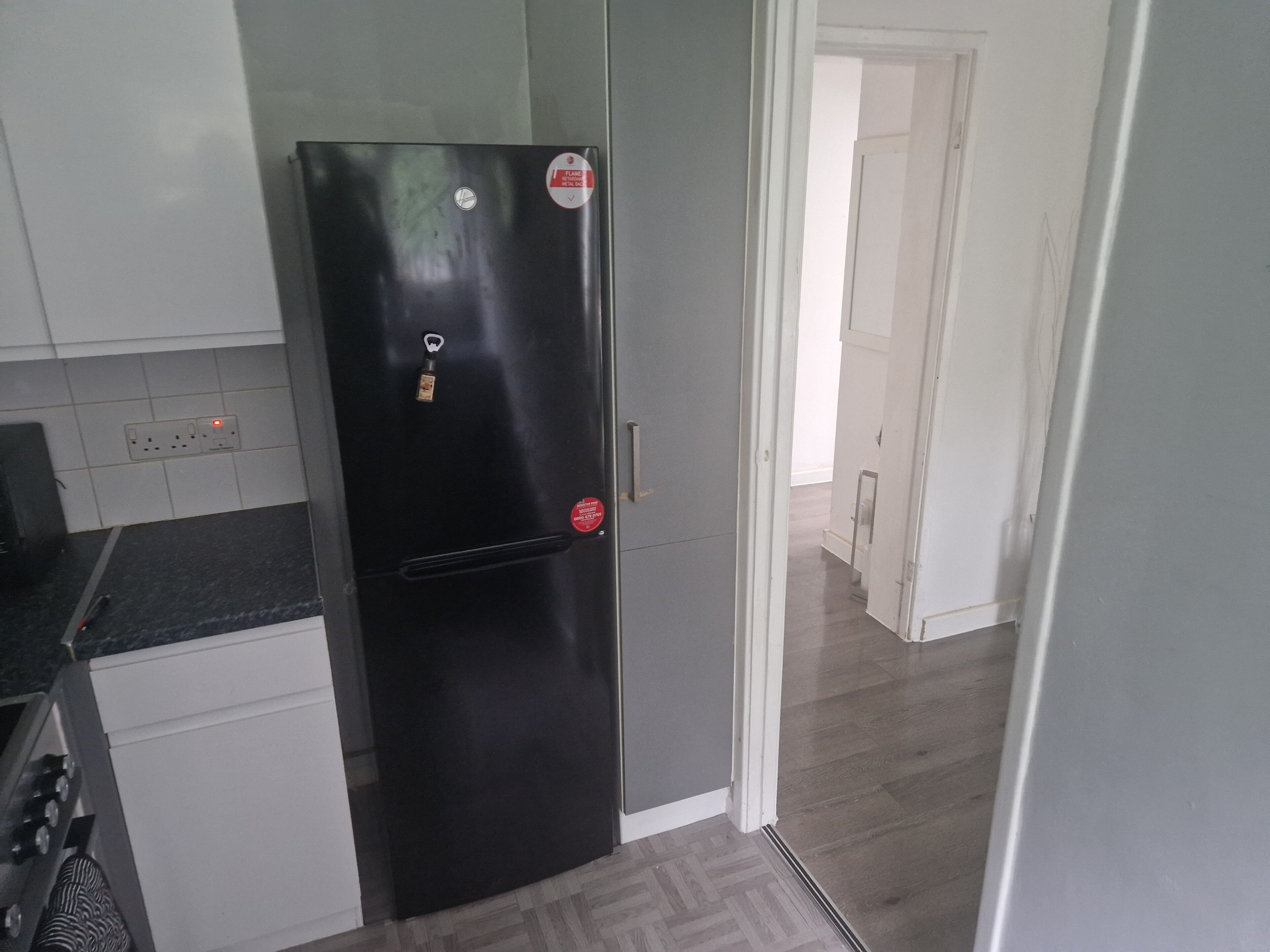 Een keuken met een zwarte koelkast, witte kasten en een betegelde spatwand.