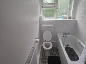 A bathroom with a toilet, a bathtub, and a window with a view of greenery outside.