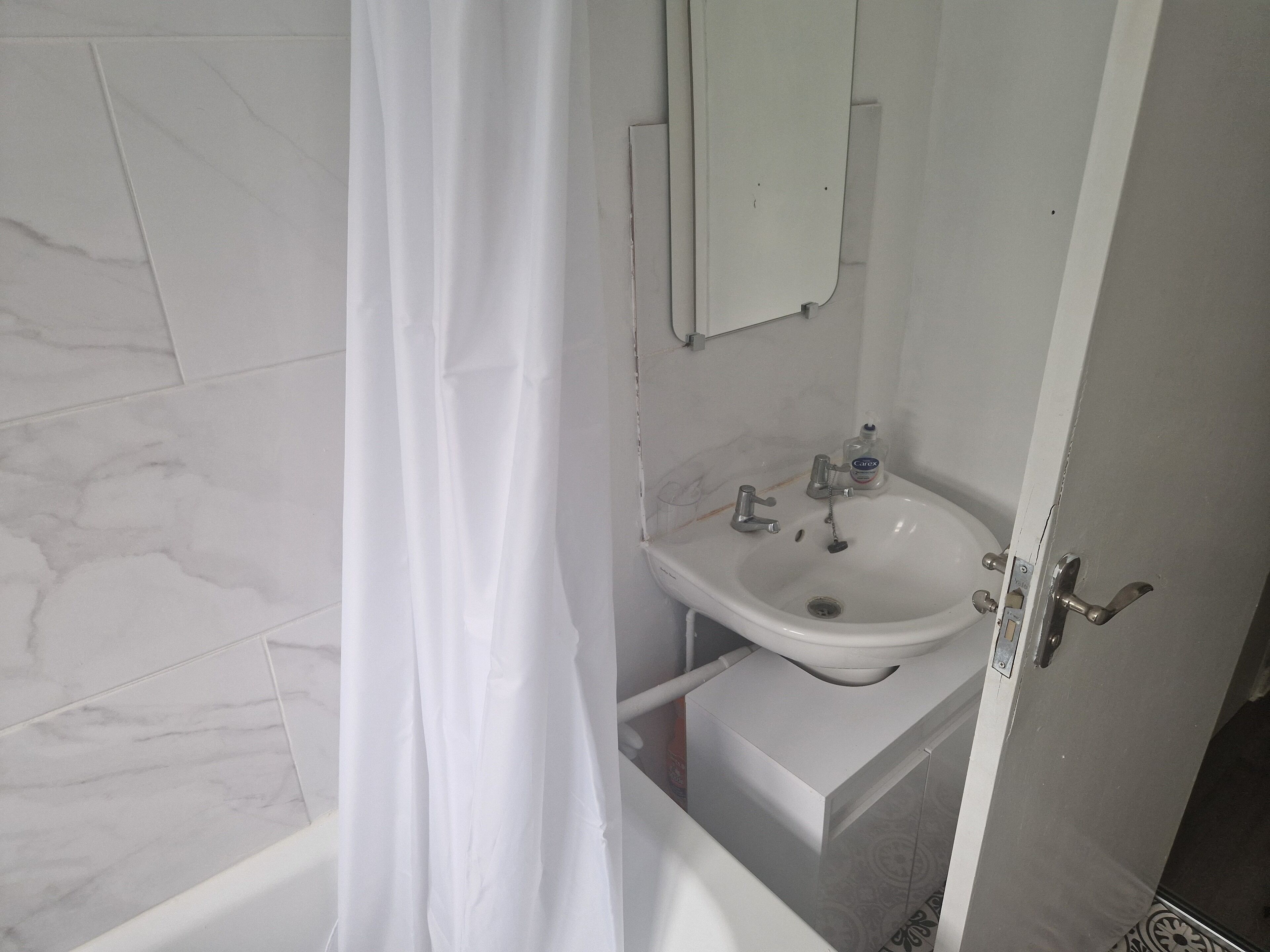 Un baño con lavamanos blanco, un espejo encima y una cortina de ducha.