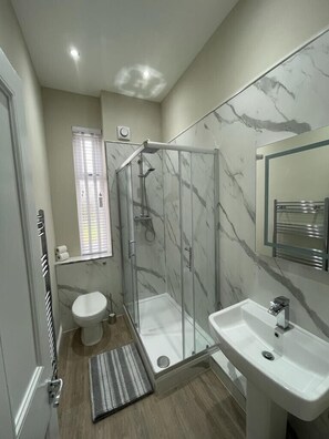 Un baño moderno con cabina de ducha de vidrio, inodoro y lavamanos.