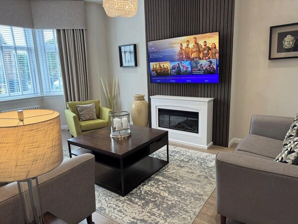 Una sala de estar moderna con chimenea, televisor de pantalla plana en la pared y un área de descanso confortable con sofá y sillones.