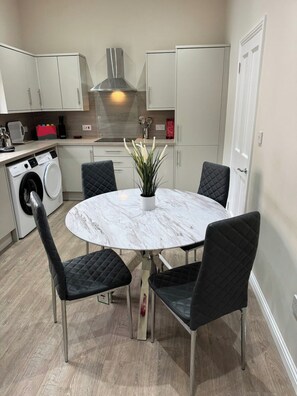 Cocina moderna con una isla central, electrodomésticos integrados y un comedor con una mesa de mármol y sillas negras.
