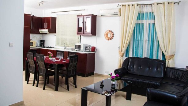 A compact living space with a dining area, a kitchenette, a black leather sofa, and a window with curtains.