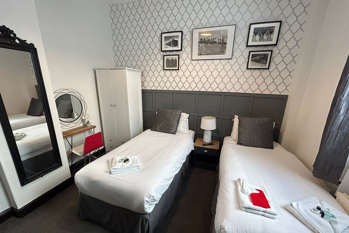 Une chambre d’hôtel avec deux lits, une armoire, un miroir et un mur orné de tableaux.