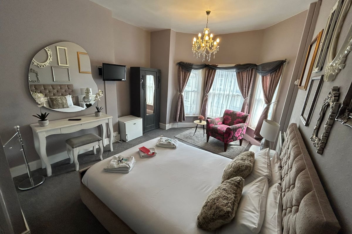 Une chambre d’hôtel avec un grand lit, un bureau, une chaise, une télévision et un lustre.