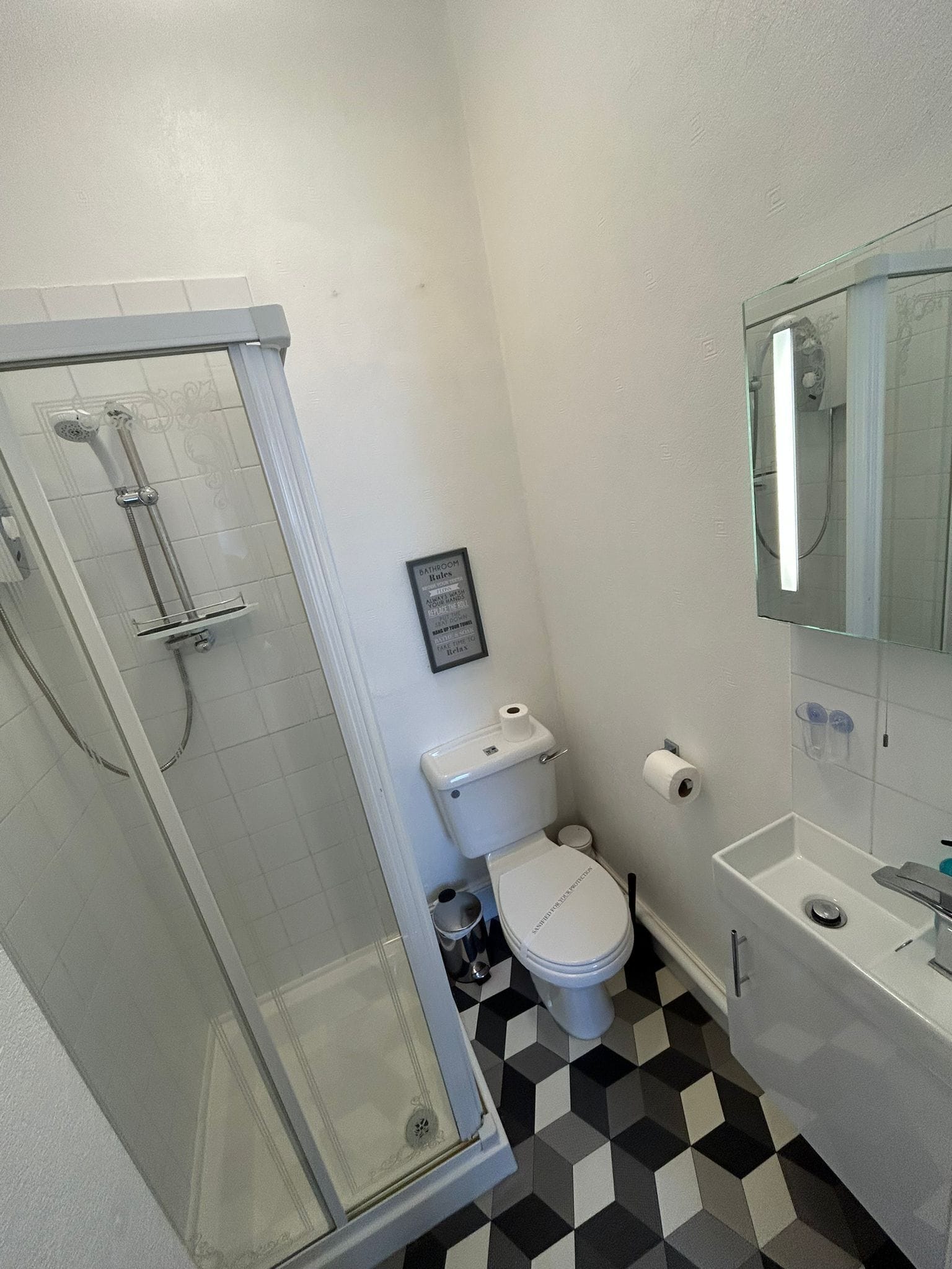 A bathroom with a glass-enclosed shower, a toilet, and a sink with a mirror above it.