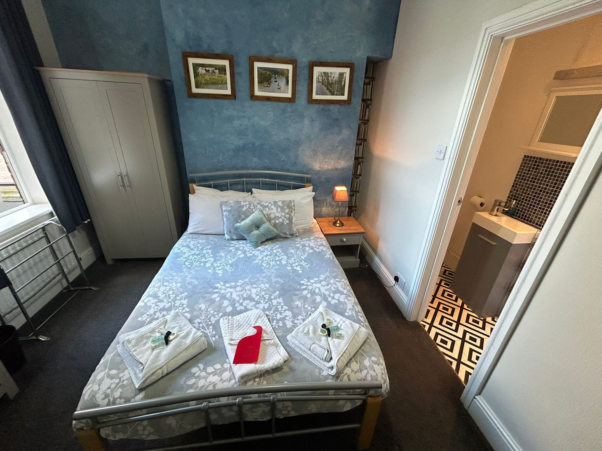A neatly arranged bedroom with a bed, bedside tables, a wardrobe, and a bathroom visible through an open door.