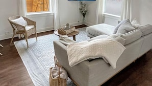 A living room with a grey sofa, a wicker chair, a small round table with a vase, and a painting on the wall. - Best neighborhood in SA! Near it all, food & fun!
 (San Antonio)