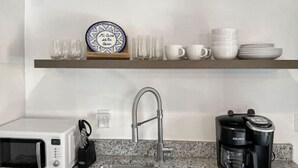 A kitchen with a double sink, a microwave, a coffee maker, and a shelf with cups and a plate. - Best neighborhood in SA! Near it all, food & fun!
 (San Antonio)