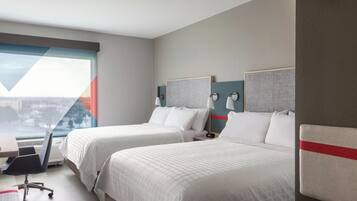 A hotel room with two beds, a desk, a chair, and a view of a cityscape.