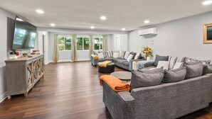 A spacious living room with a grey sofa set, a wooden cabinet, and a flat-screen TV.