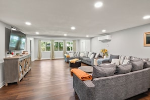 A spacious living room with a grey sofa set, a wooden cabinet, and a flat-screen TV.
