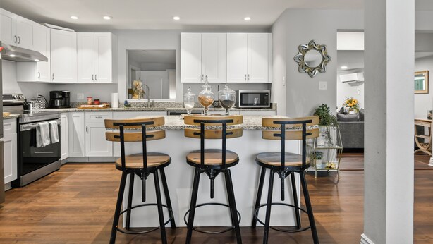 A modern kitchen with white cabinets, a central island with bar stools, and a microwave.