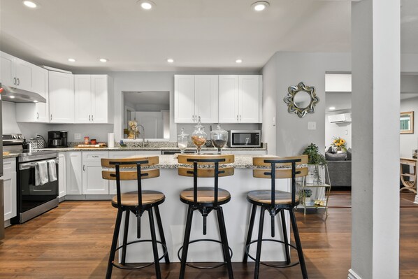 A modern kitchen with white cabinets, a central island with bar stools, and a microwave.