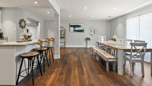 A modern kitchen with a central island, bar stools, and a dining area with a wooden table and benches.