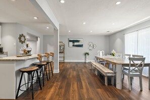 A modern kitchen with a central island, bar stools, and a dining area with a wooden table and benches.