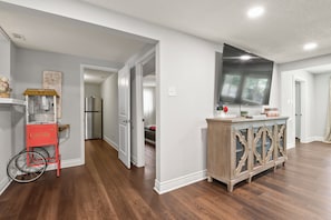 A modern kitchen with wooden flooring, a popcorn cart, and a large flat-screen TV mounted above the counter.