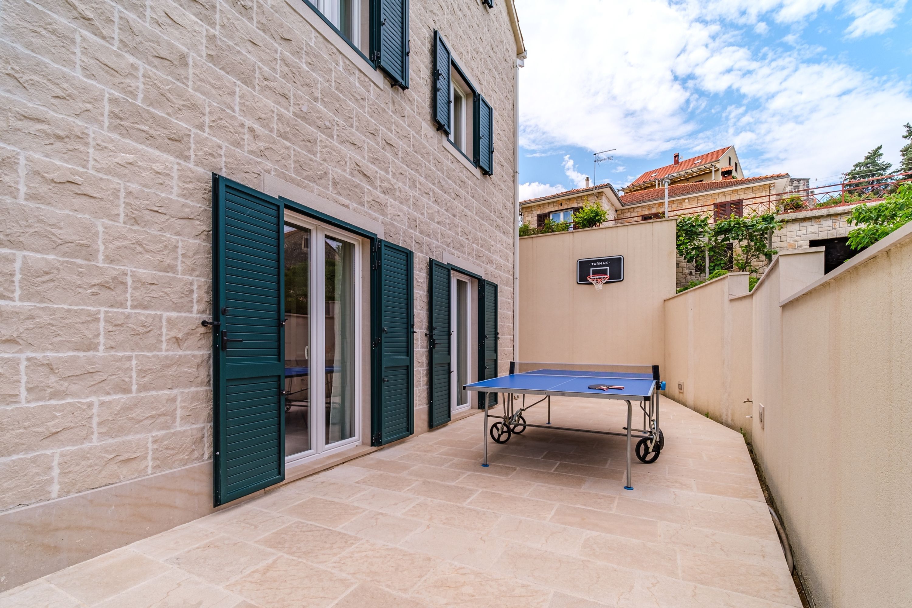 Un patio con mesa de ping pong, aro de baloncesto y un edificio de piedra con contraventanas.
