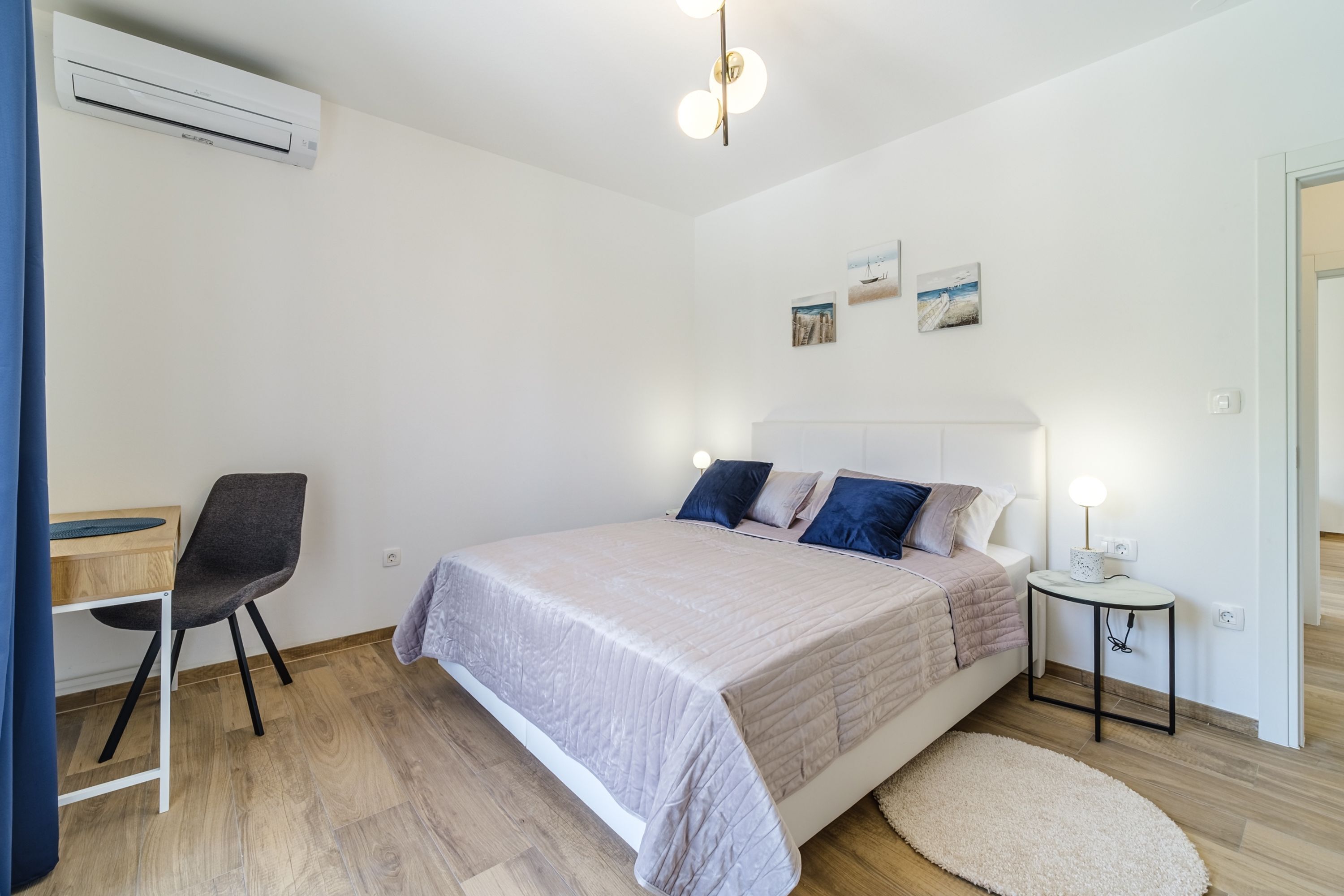 Quarto com cama, mesa de cabeceira, luminária e aparelho de ar condicionado na parede.