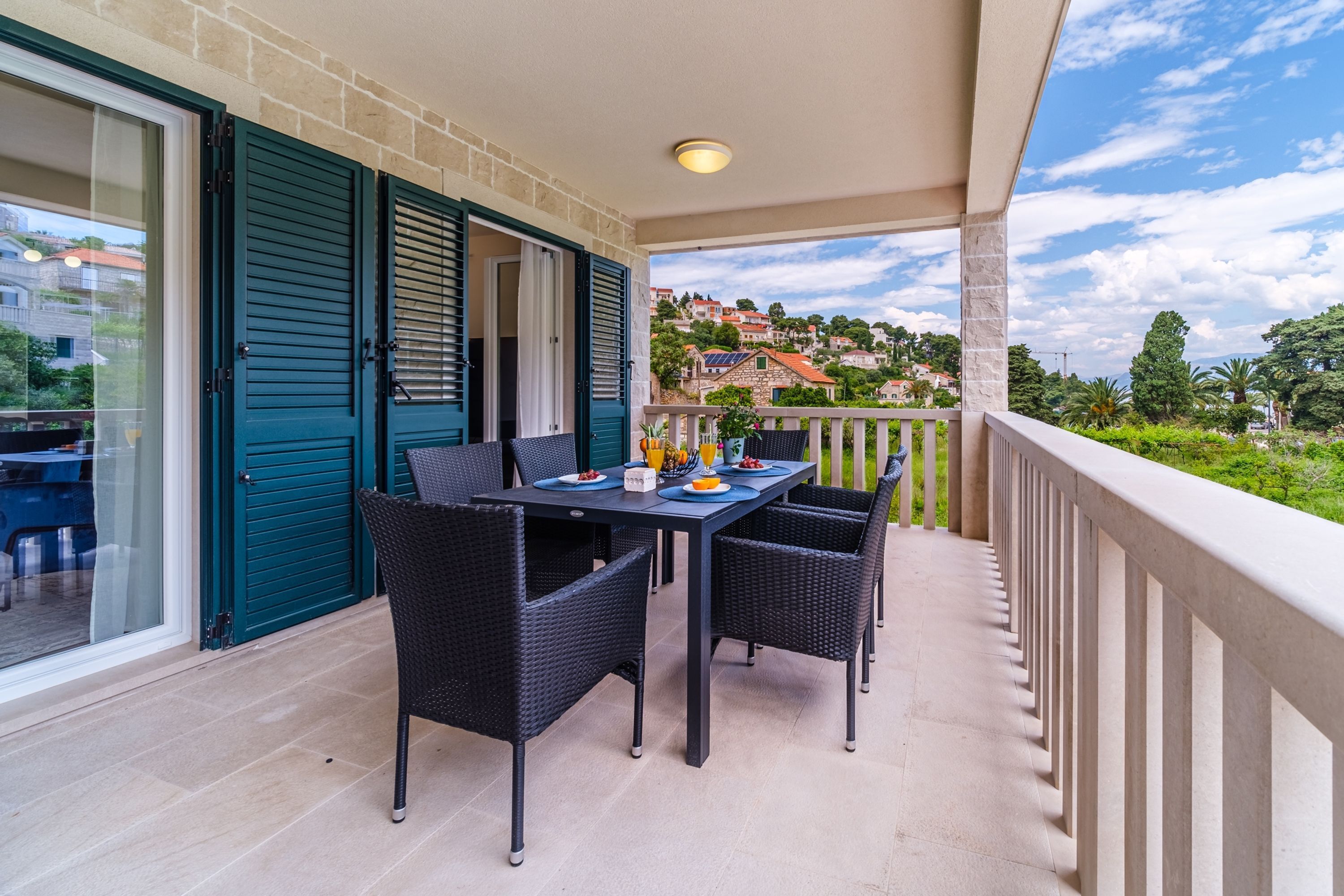 Un balcon avec une table dressée pour deux personnes, une porte-fenêtre coulissante et une vue sur une colline parsemée de bâtiments.