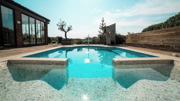 Una piscina rectangular amb una superfície d'aigua blava i cristal·lina, envoltada per un solàrium de pedra.