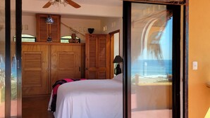 Un dormitorio con cama, armario de madera y vista a la playa a través de un ventanal corredero.