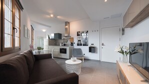 A modern living room with a sofa, a coffee table, and a TV. There is a kitchen area with cabinets and a stove. - Loft Gran Canaria (Arucas)