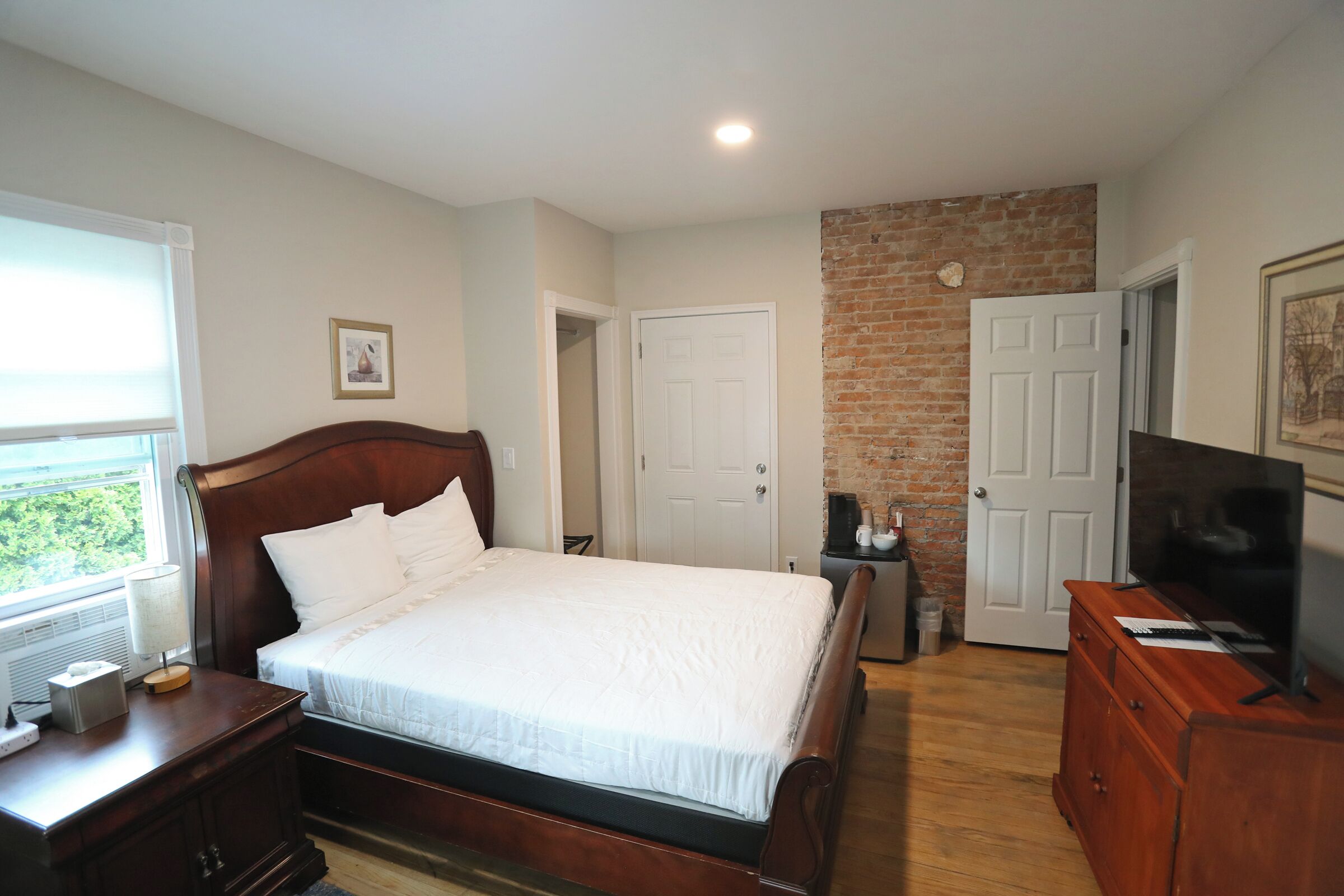 A bedroom with a wooden bed, a dresser, a television, and a brick accent wall.