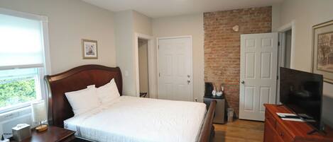 A bedroom with a wooden bed, a dresser, a television, and a brick accent wall.