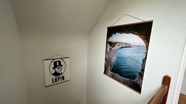 Uma escadaria com corrimão de madeira e um quadro pendurado na parede, retratando uma paisagem costeira.
