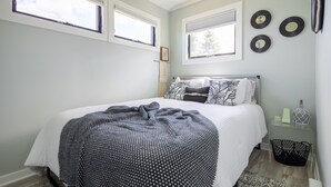 Une chambre à coucher avec un lit, une fenêtre, une étagère fixée au mur et une lampe sur pied.