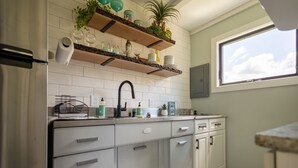 Une cuisine avec des armoires blanches, un robinet noir et des étagères ornées de plantes et d’ustensiles de cuisine.