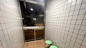 Un baño pequeño con paredes de azulejos, dos taburetes verdes, una ventana y un espejo.