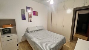 Un dormitorio con una cama, un armario, una estantería con objetos decorativos y un ventilador de techo.