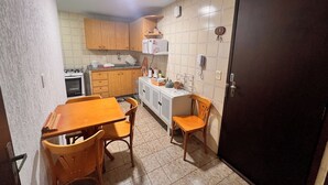 Cocina compacta con armarios de madera, estufa y microondas. Hay una mesa de comedor con sillas y un refrigerador pequeño.