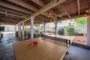 An outdoor ping pong table with a red paddle, under a wooden pergola with string lights. - 2 homes + pool & hot tub. Walk to beach! (Galveston)