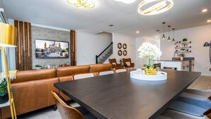 Un salon moderne avec une table à manger en bois foncé, un canapé en cuir et un téléviseur fixé au mur.