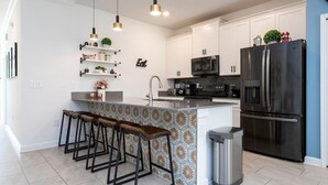 Une cuisine moderne avec des meubles blancs, un réfrigérateur en acier inoxydable et un coin bar équipé de tabourets.