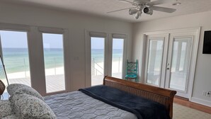 Un dormitorio con cama, ventilador de techo y vista al océano a través de amplias ventanas.